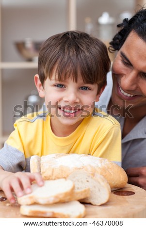 Smiling child eating bread with his father in the kitchen
