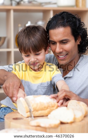 Attractive father helping his son cut some bread in the kitchen