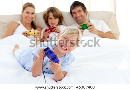 Little blond girl playing video game with her family in the bedroom