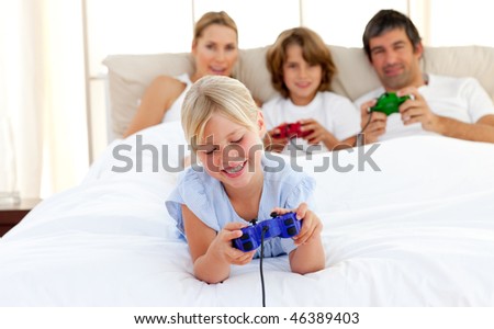 Cute blond girl playing video game with her family in the bedroom