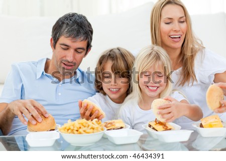 Loving family eating hamburgers sitting on sofa