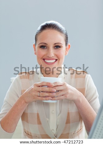 Delighted businesswoman drinking a coffee at her desk