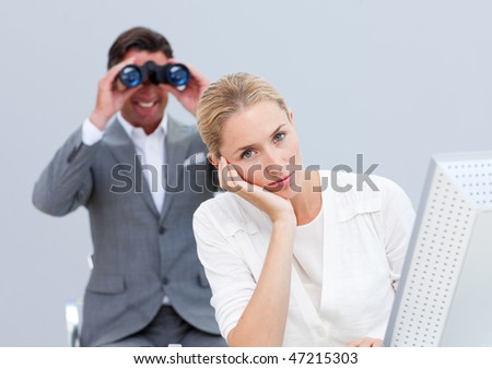 Blond businesswoman annoyed by a man looking through binoculars in the office