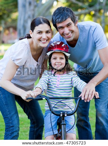 Little girl learning to ride a bike with her parents in a park