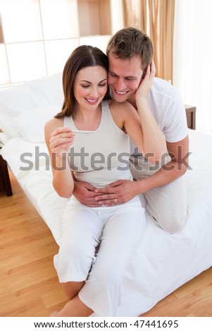 Blissful couple finding out results of a pregnancy test sitting on bed