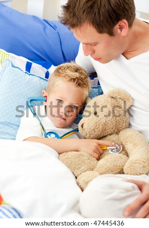 Caring father and his sick son playing with a stethoscope sitting on bed