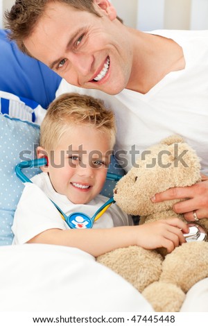 Handsome father and his sick son playing with a stethoscope sitting on bed