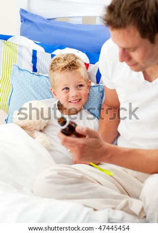 Handsome father giving cough syrup to his sick son sitting on bed