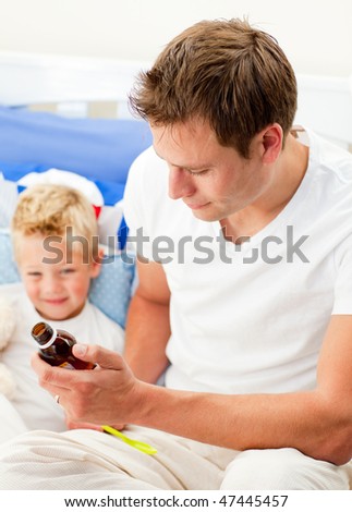 Attentive father giving cough syrup to his sick son sitting on bed