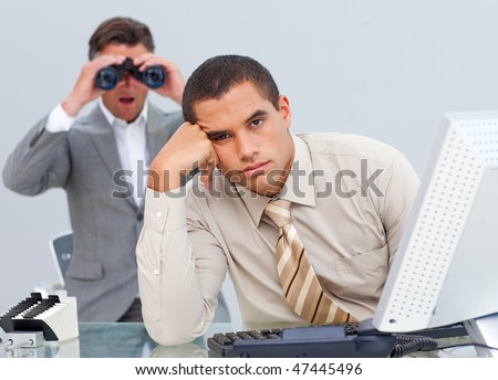 Handsome businessman getting bored and his manager looking through binoculars in the office