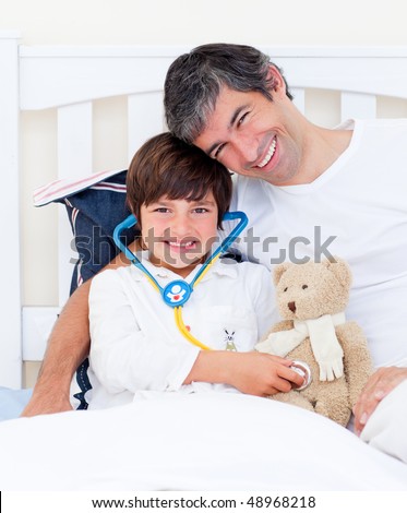 Attentive father and his sick son playing with a stethoscope sitting on a bed