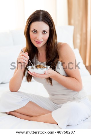 Brunette woman eating cereals sitting on bed at home