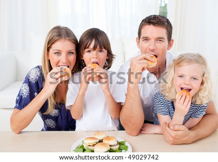 Hungry family eating burgers in the living room at home