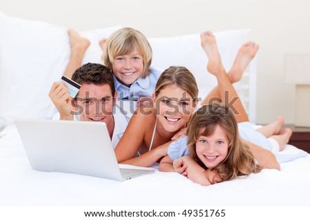 Enthusiastic family buying online lying down on bed at home