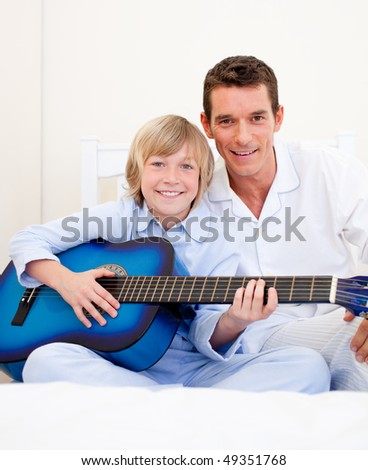 Merry little boy playing guitar with his father in the bedroom