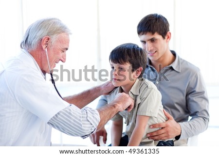 Senior doctor examining a little boy with his father at the practice