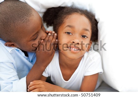 Adorable little boy whispering something to his sister under the cover