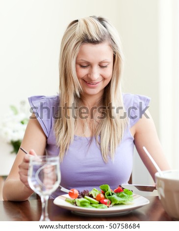 Happy young woman eating a salad in a living-room