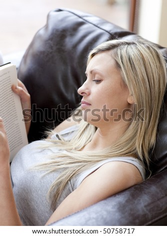 Concentrated woman reading a book sitting on a sofa in a living-room