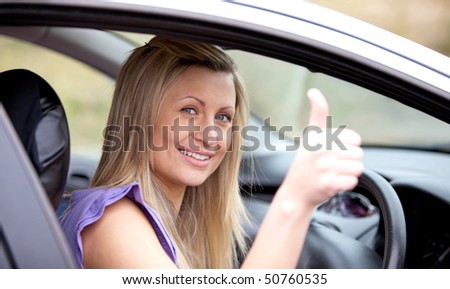 Smiling female driver with thumb up sitting in her car