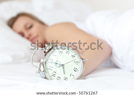 Young woman holding an alarm clock and sleeping on her bed