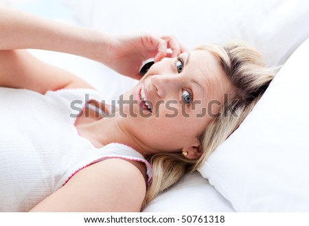 Beautiful young woman on phone lying on her bed at home