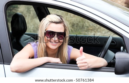 Happy female driver wearing sunglasses with thumb up sitting in her car