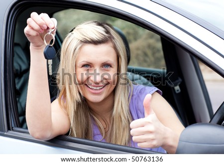 Charming female driver showing a key with a thumb up after buying a new car