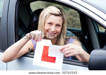 Cheerful young female driver tearing up her L sign sitting in her car