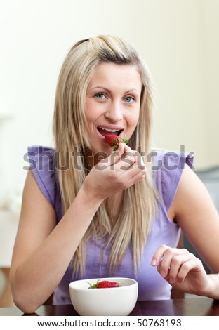 Portrait of an attractive woman eating a strawberry in a living-room