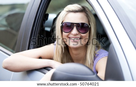 Jolly female driver wearing sunglasses sitting in her car smiling at the camera