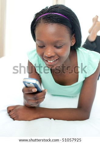 stock photo Cute teen girl using a mobile phone lying on her bed at home