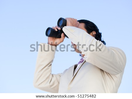 Portrait of an handsome business man looking through binoculars against a blue sky background