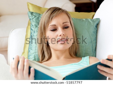 Portrait of a beautiful woman reading a book lying on a sofa