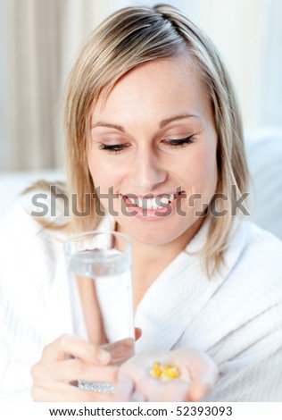 Sick young woman holding a glass of water and pills sitting on a sofa