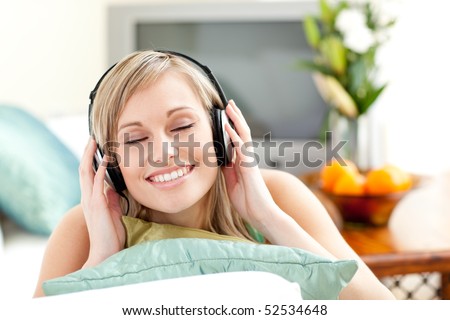Delighted young woman listening music with headphones lying on a sofa