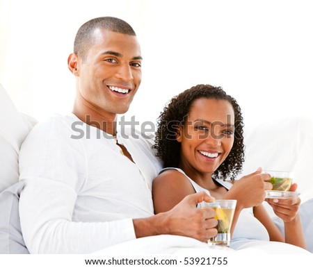 Happy couple drinking a cup of tea lying on their bed at home