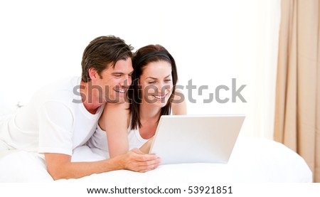 Cheerful couple using a computer lying on their bed at home