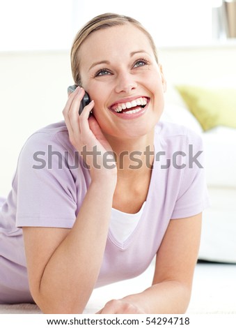 Delighted woman talking on phone lying on the floor at home