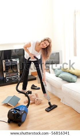 Charming woman in her chaotic living room with a vacuum cleaner