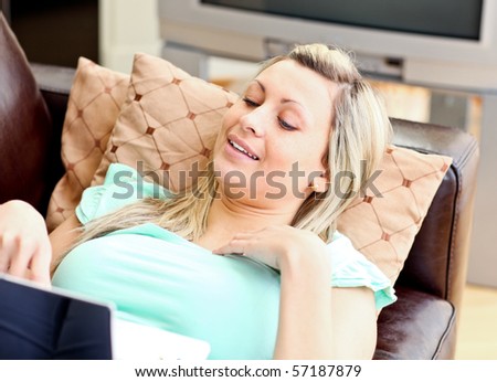 Beautiful woman lies on brown sofa at home and works at laptop