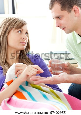 Loving boyfrieng giving his sick girlfriend pills lying on a sofa