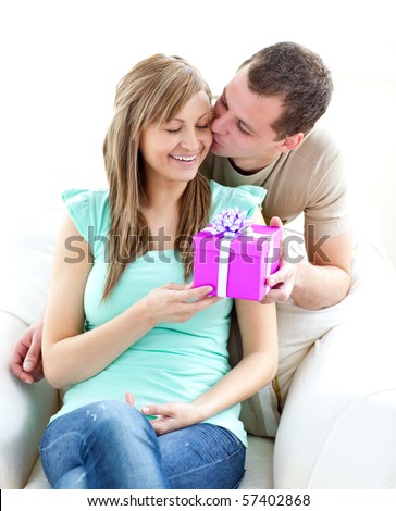 Attractive boyfriend giving a present and a kiss to his glowing girlfriend against white background