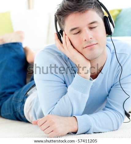 Relaxed man lying on the floor listening to music with headphones closed eyes in the living room