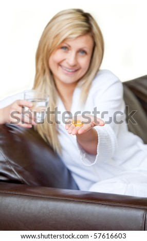 Happy woman  holding pills and a glass of water smiling at the camera sitting on the sofa