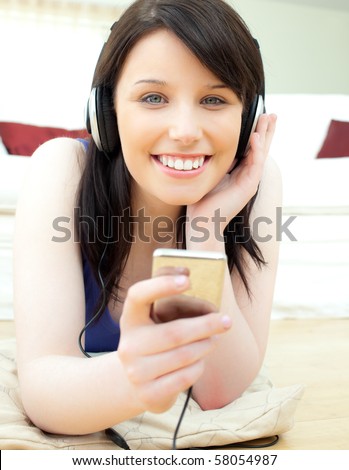Glowing young woman listen to music lying on the floor in the living room