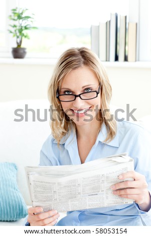 Charming businesswoman reading the newspaper sitting on the sofa at home