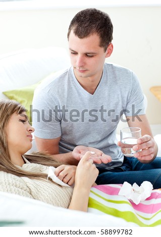 Caring man giving his sick girlfriend pills and water in the living room