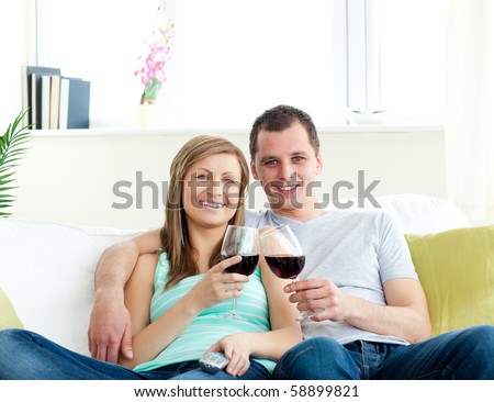 Young embracing  couple sitting on the sofa drinking wine at home