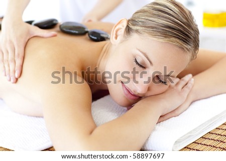 Bright young woman enjoying a back massage with hot stone in a spa center